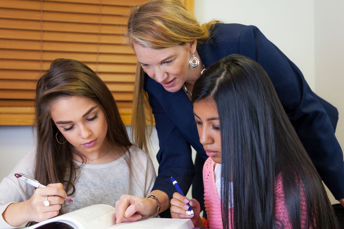 Una docente acompaña a dos estudiantes que leen y escriben en su libro