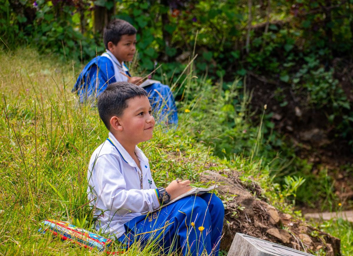 Dos estudiantes con uniforme escolar escriben en sus cuadernos sentados en el campo